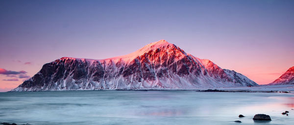 Scenic view of sea by snowcapped mountain against sky during sunset