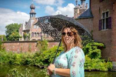 Portrait of smiling woman holding umbrella while standing in city 