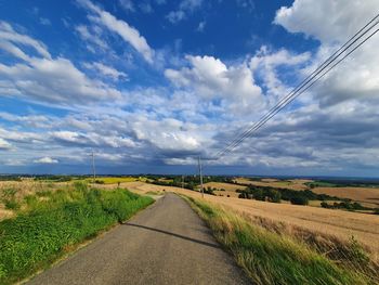 Empty road amidst field against sky