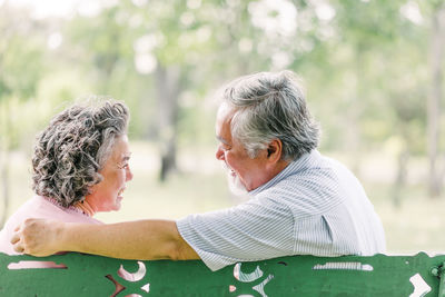 Side view of happy senior couple talking while sitting on bench in park