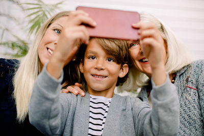 Smiling boy taking selfie with mother and grandmother in mobile phone