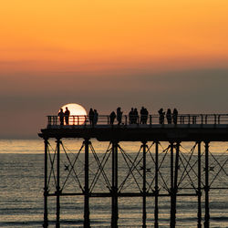 Silhouette people by sea against sky during sunset