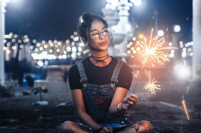 Portrait of smiling young woman sitting in park at night