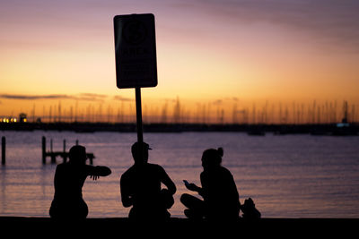 Silhouette friends by lake during sunset