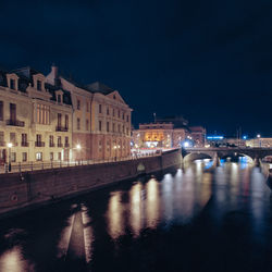 Illuminated buildings by river against sky in city at night