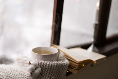 Cup of hot tea and an open book with a warm sweater on a vintage wooden windowsill
