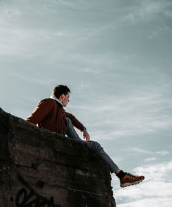 Low angle view of man sitting on rock against sky