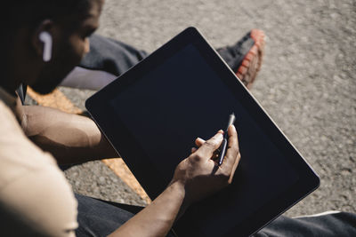 Young man using tablet through digitalized pen while sitting on sports court