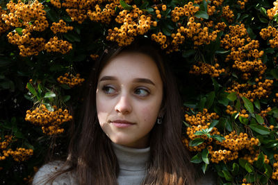 Close-up of thoughtful young woman standing against orange berries on plant