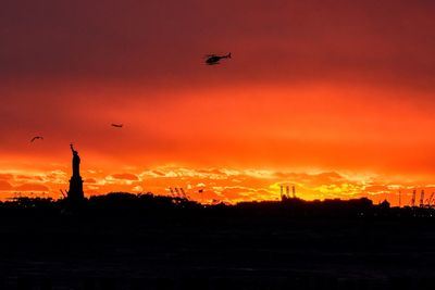 Silhouette airplane flying against orange sky