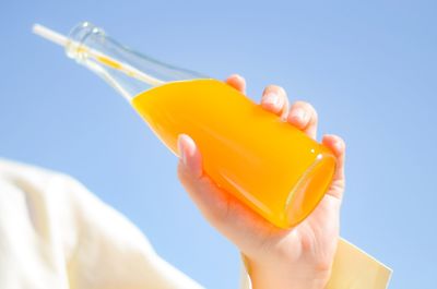 Close-up of hand holding yellow bottle against blue sky