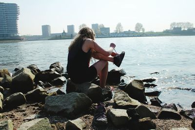 Rear view of couple sitting on rock by sea