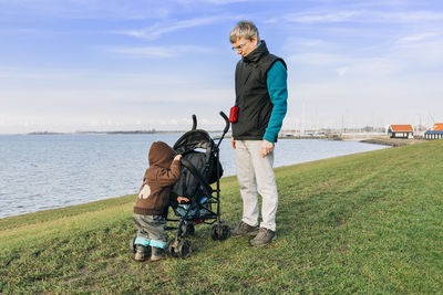 Grandfather with daughter standing on shore against sky