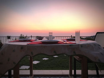 Empty chairs and tables by sea against sky during sunset