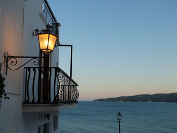 Illuminated street light by sea against clear sky