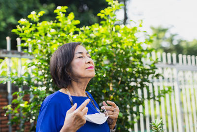 Senior woman holding protective mask in her hand standing in the garden for fresh air.