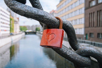 Close-up of padlock on chain against buildings and canal in city