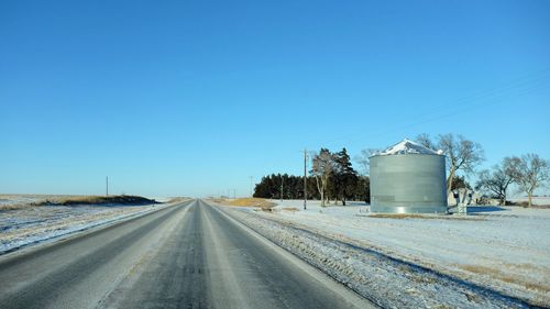 Empty road by field against blue sky during winter