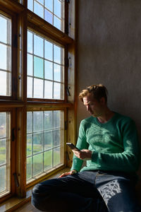 Man looking away while sitting on window at home