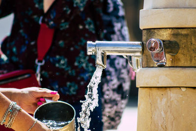 Midsection of woman filling water metal container outdoors