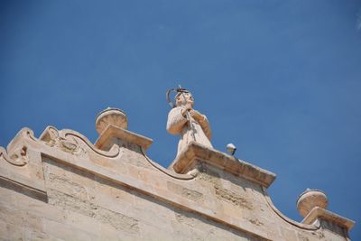 Low angle view of statue against building against blue sky