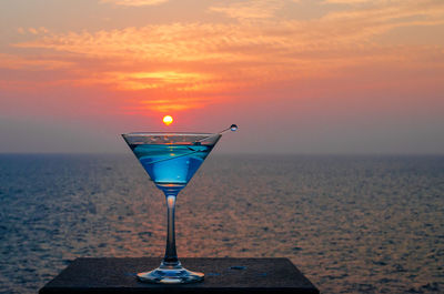 Close-up of wine glass on beach against sky during sunset