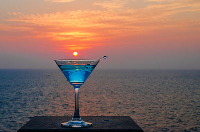 Close-up of martini glass against sea during sunset