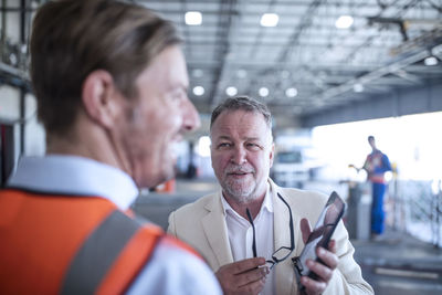 Businessman showing cell phone to man in reflective vest in industrial hall