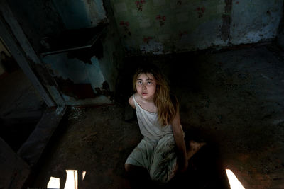 Frightened teenage girl sitting on the floor in an old house