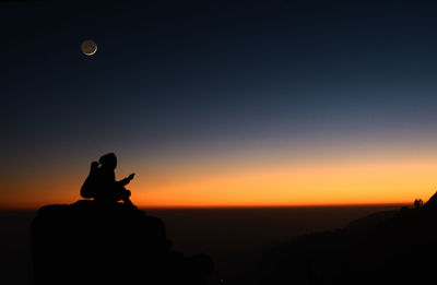 Silhouette man on rock against sky during sunset