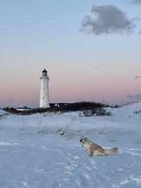 Lighthouse by sea against sky during sunset