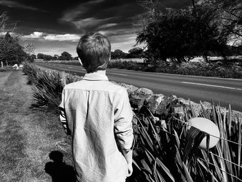 Rear view of man standing by road against sky