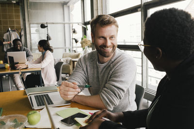 Smiling businessman discussing with businesswoman while sitting at desk in office