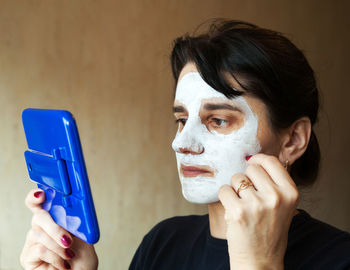 Woman wearing facial mask while looking in hand mirror at home