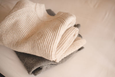 Stack of knitted wool textile sweaters clothes on white blanket in bed at home room close up.