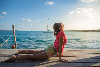 Rear view of woman sitting on pier over sea against sky