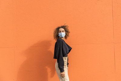 Portrait of woman standing against orange wall