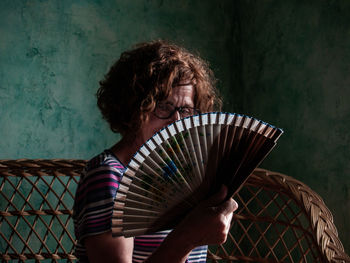 Portrait of woman holding hand fan while sitting on seat at home