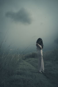 Woman standing on field by sea against sky