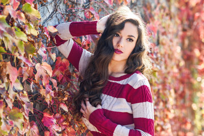 Beautiful woman standing by ivies on wall during autumn