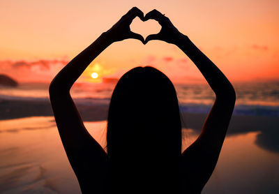 Low angle view of silhouette woman holding heart shape
