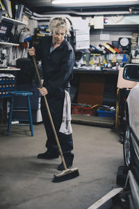 Full length of female mechanic sweeping in auto repair shop