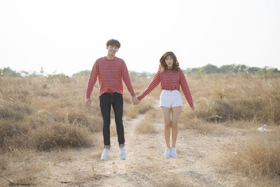 Full length portrait of couple holding hand standing on field