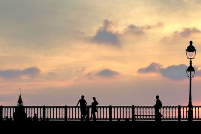Silhouette people standing on railing against sky during sunset