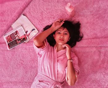 Portrait of young woman lying on pink rug at home