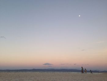 Father with son at beach against sky during sunset