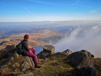 Woman sitting on rock looking at mountains against sky