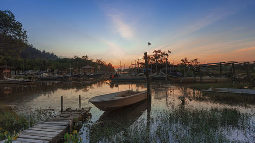 Boats moored in river at sunset