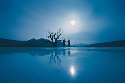 Silhouette couple standing on frozen lake against sky at dusk