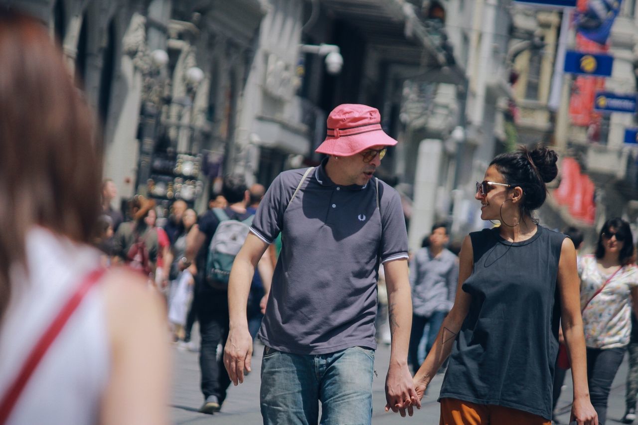 real people, casual clothing, incidental people, lifestyles, city, young adult, architecture, hat, people, focus on foreground, leisure activity, street, cap, day, young men, men, adult, built structure, women, market